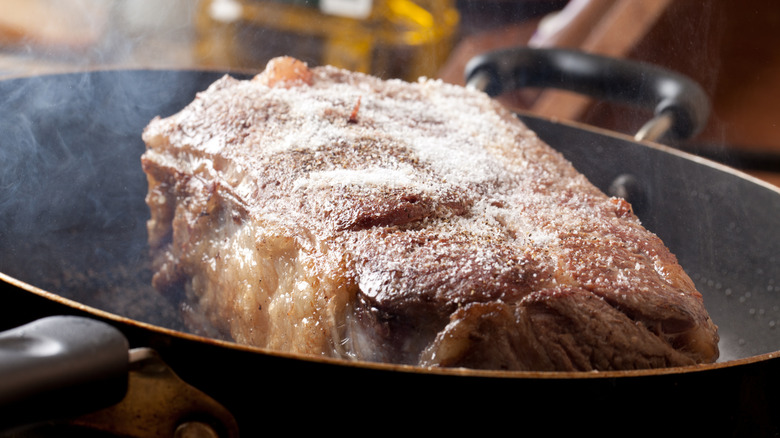 A slab of chuck roast is being seared on a hot pan on the stove