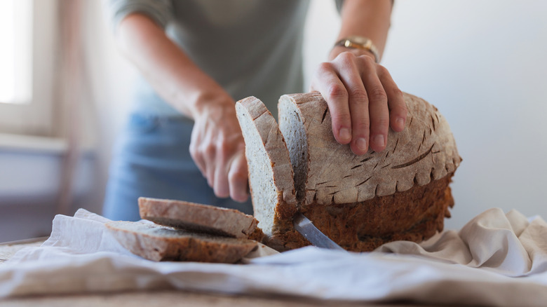 Hand slicing a load of bread on tablecloth