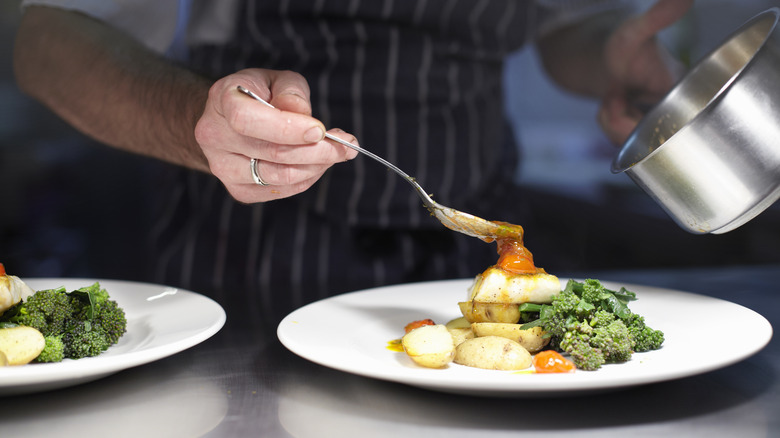 Chef spooning sauce on plated dish