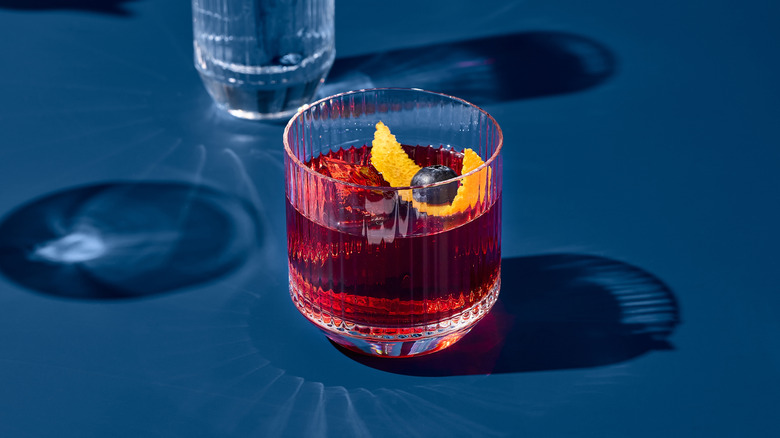 Red cocktail in glass with lemon rind and blueberry garnish