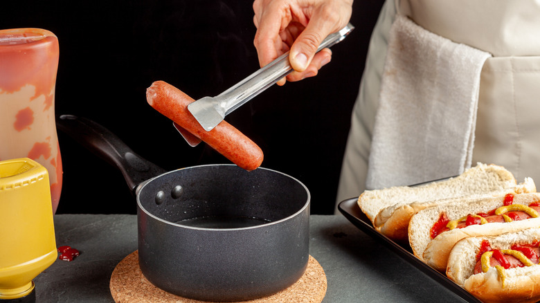 A home cook takes a hot dog out of a pot of warm water