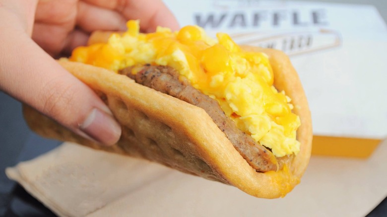 A hand holding a Waffle Taco from Taco Bell