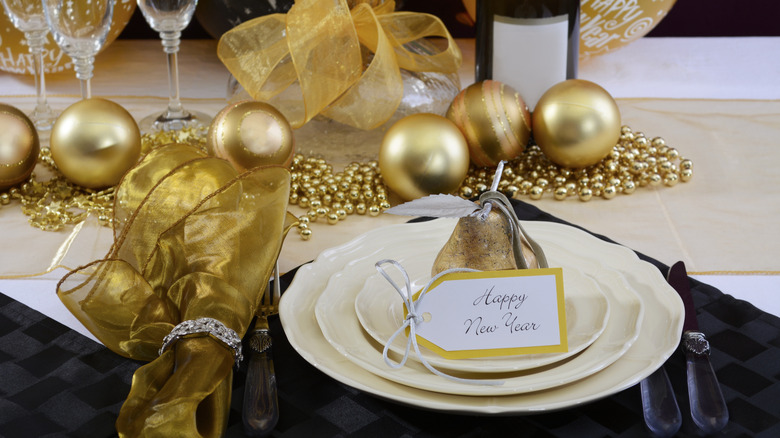 "Happy New Year" table setting with white plates, a gold napkin, and gold decorative balls