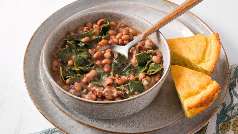 Black-eyed peas with collard greens in a light gray bowl with two small pieces of cornbread on the side