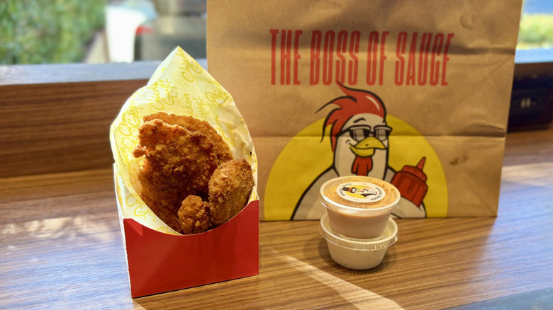Chicken Guy! chicken tenders in their box sit next to dips and the bag they came in