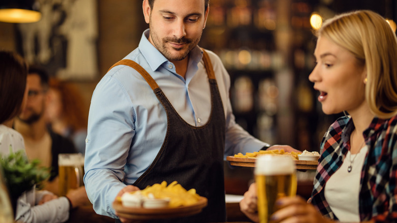 A waiter sets a dish on a table in front of a female customer