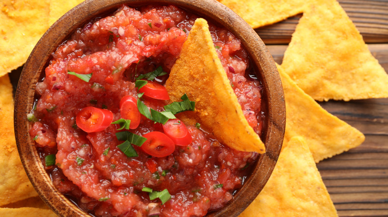 Closeup of salsa in a wooden bowl with a tortilla chip dipped into it and other chips surrounding the dish
