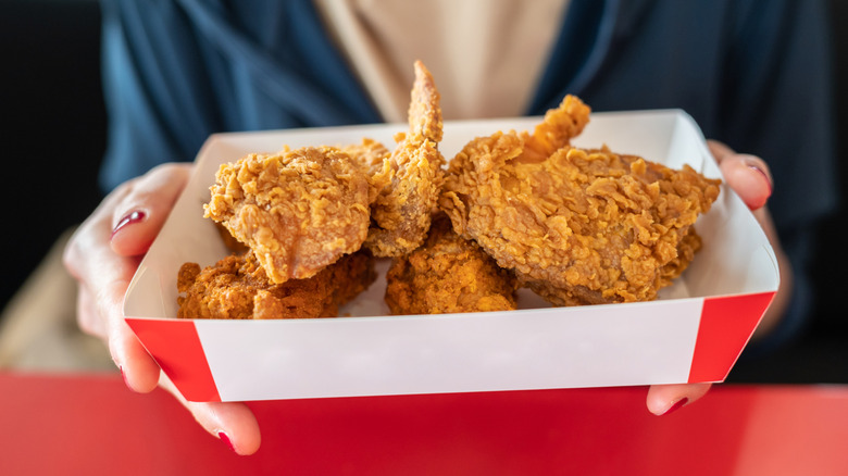 Hands holding paper takeout basket of fried chicken