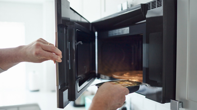 Person putting frozen meal into microwave