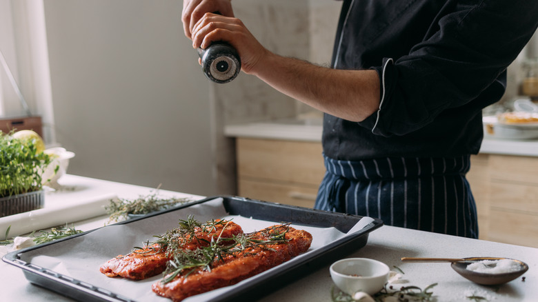 Person salting seafood on baking tray