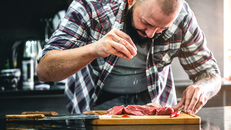 Person salting red meat on wooden slab