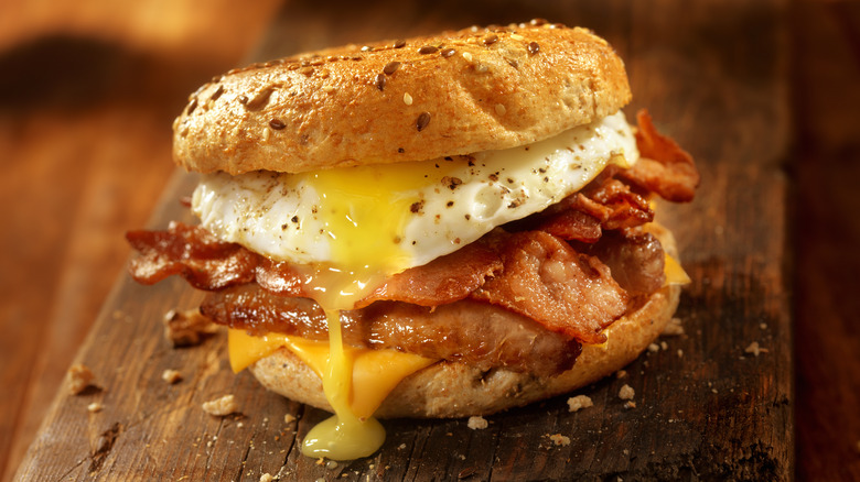 bacon egg and cheese breakfast sandwich on a bagel on a wooden cutting board