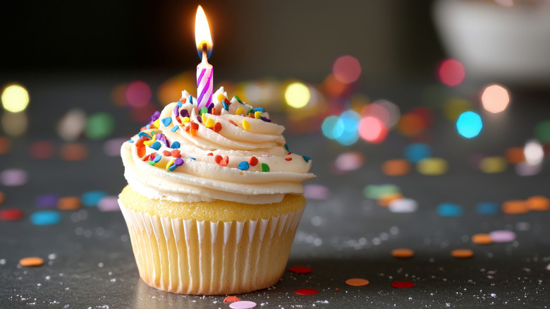 Single cupcake with lit candle and sprinkles