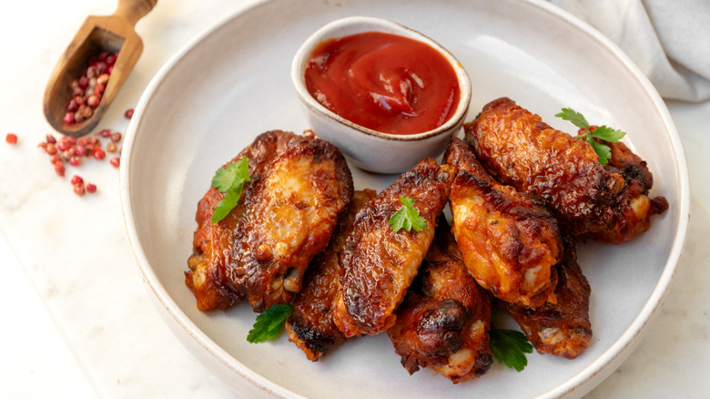 A plate of chicken wings and sauce on a white table