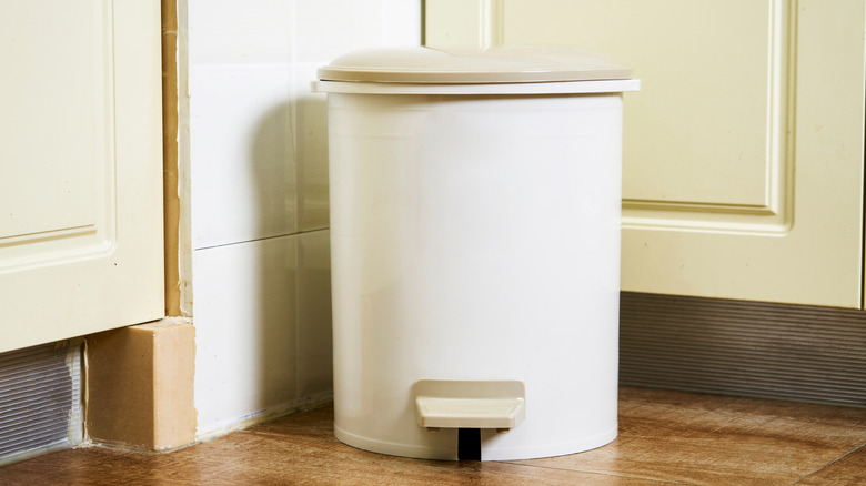 Trash can in the corner of a kitchen.