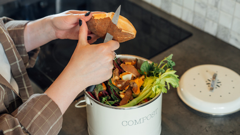 A homeowner peeling a sweet potato into a kitchen compost bin.