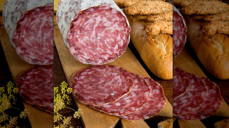 A platter of finocchiona, sliced and in a sausage roll, sits next to bread and seeded breadsticks.