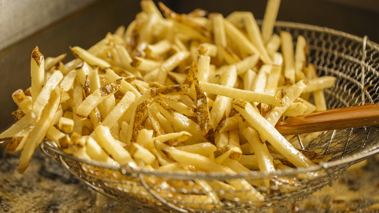 A spider tool holds french fries above some hot oil.