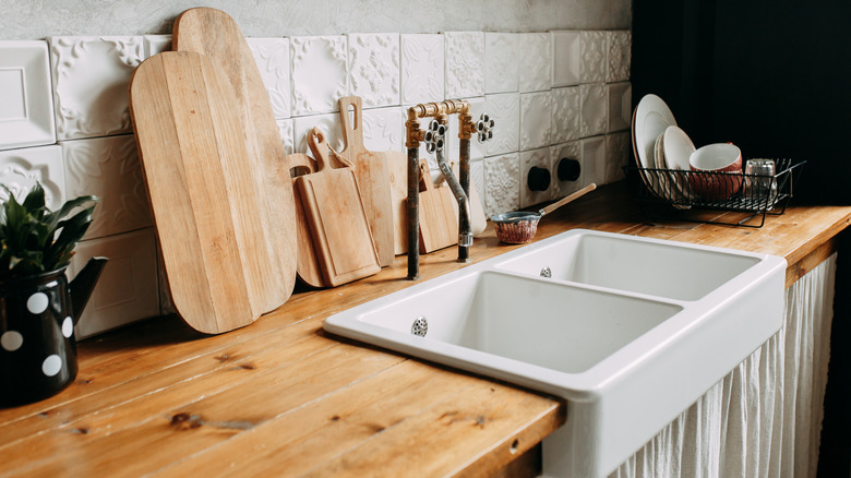 A wooden kitchen countertop with a porcelain sink is decorated with wood cutting boards