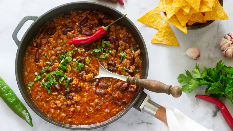 pot of chili next to chips and hot peppers