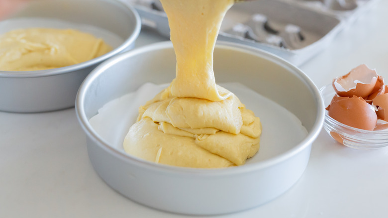 Pouring vanilla cake batter into round metal pan lined with wax paper