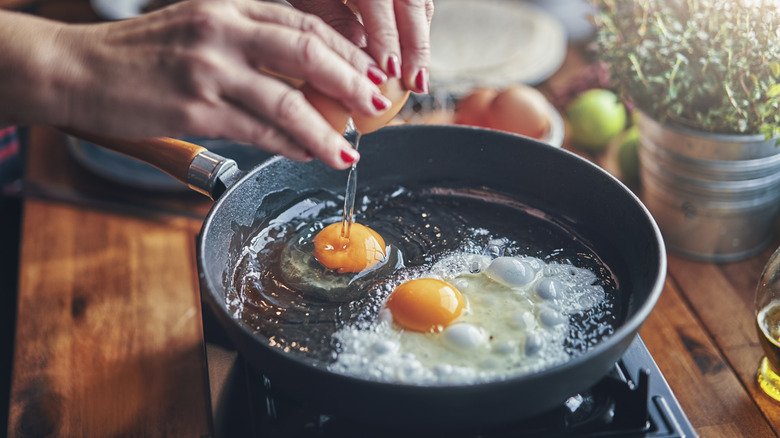 Hands crack eggs into sizzling pan
