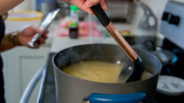 A cook stirring a pot of pho broth on a residential stovetop