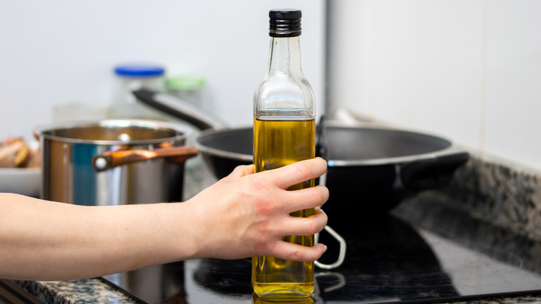 Hand holding olive oil on stove top