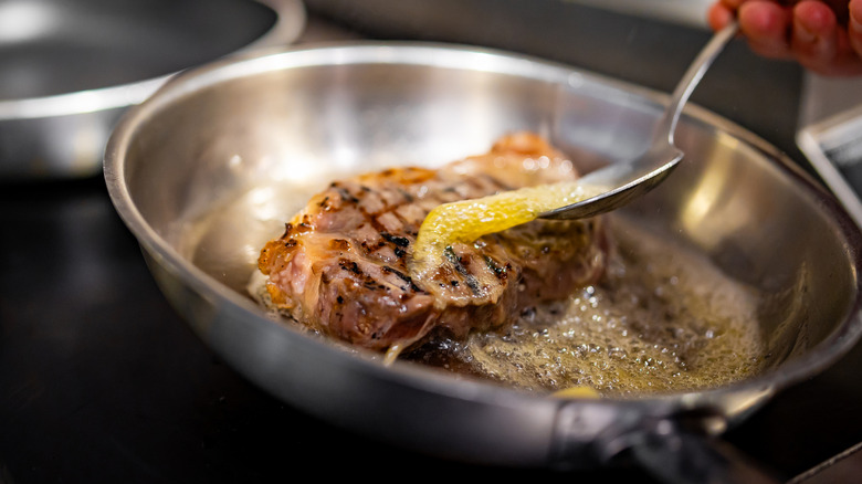 A chef bathes a steak in hot butter in a skillet