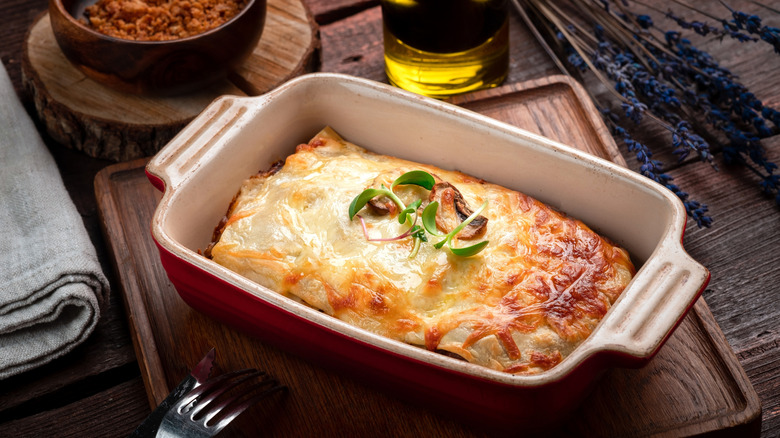 lasagna in a baking dish on a wooden cutting board