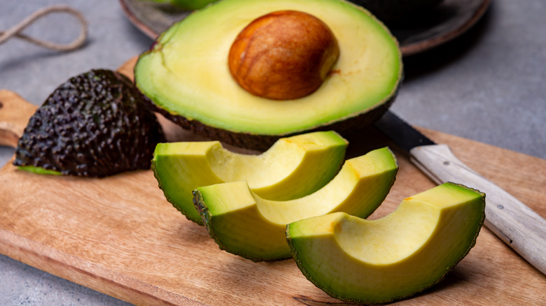 Ripe green cut avocado half with pit and slices on cutting board