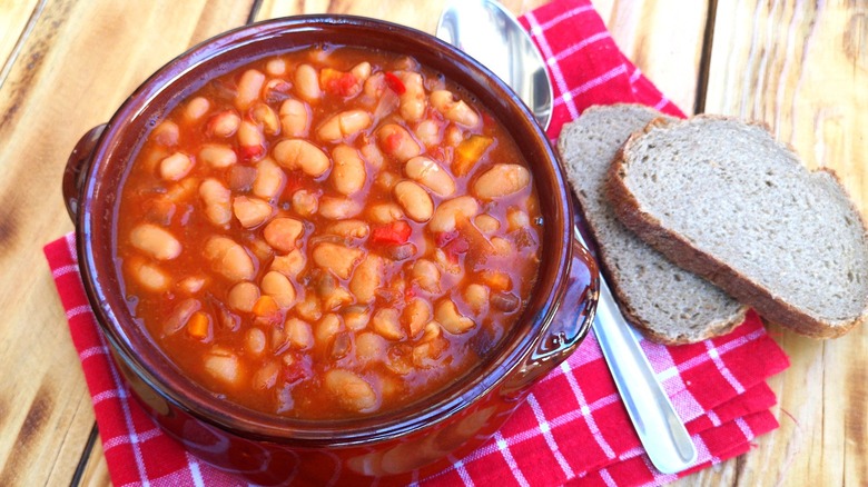 Red enamel dish full of baked beans next to two slices of brown bread