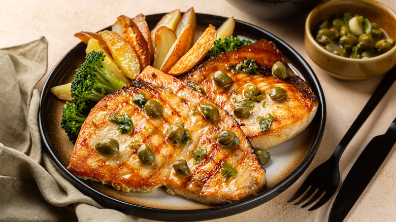 Swordfish served in a restaurant with lemon and capers, broccoli and potatoes on a black plate