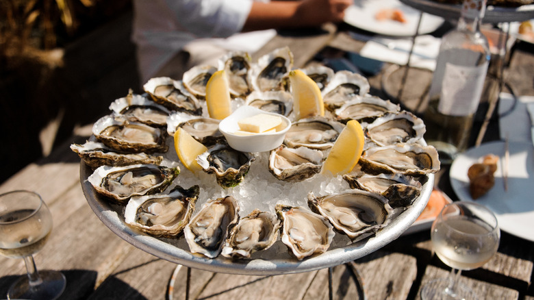 A tray of oysters served over ice with lemon wedges and a ramekin of butter.