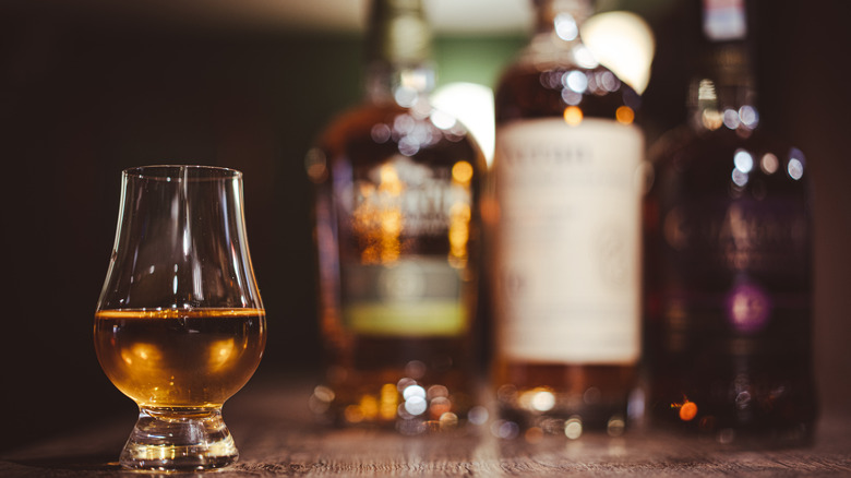 A whiskey glass with bottles in the background.