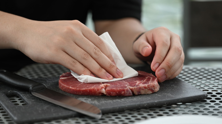 Person pats steak dry with a paper towel