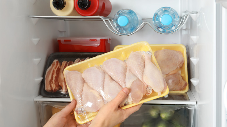 hands storing raw drumsticks in back of the fridge