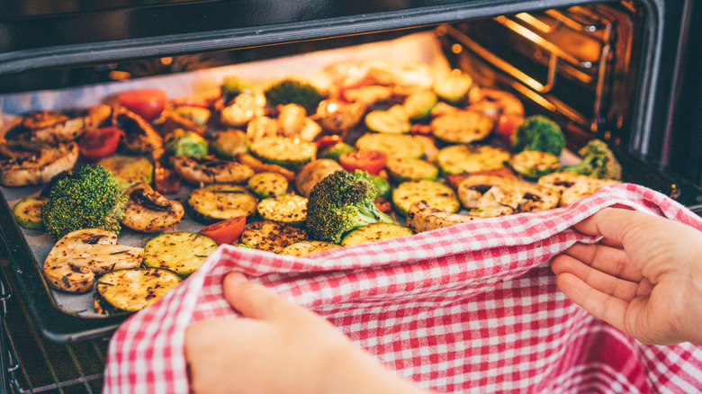 Chef pulling a tray of assorted roasted vegetables from the oven