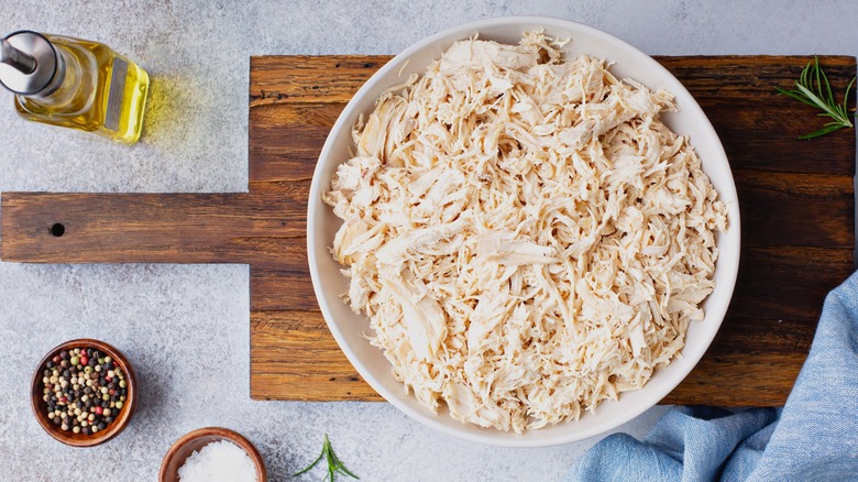 Shredded chicken sits in a white bowl on a wooden cutting board