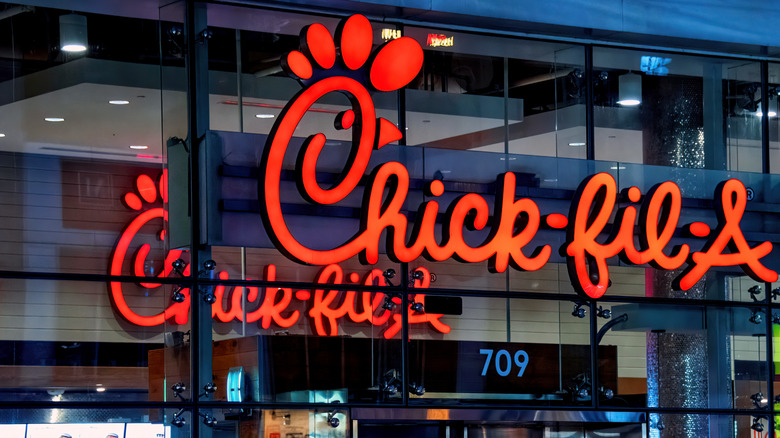 Close up of Chick-fil-A's sign on glass windows with another indoor sign in the background