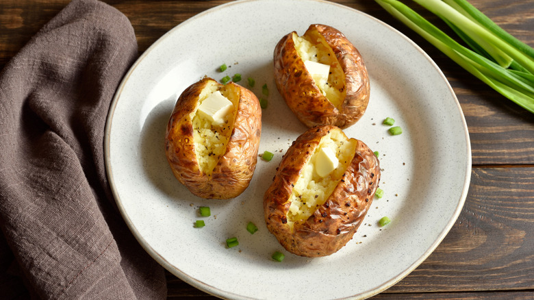 Baked potatoes on a plate with butter and seasonings.