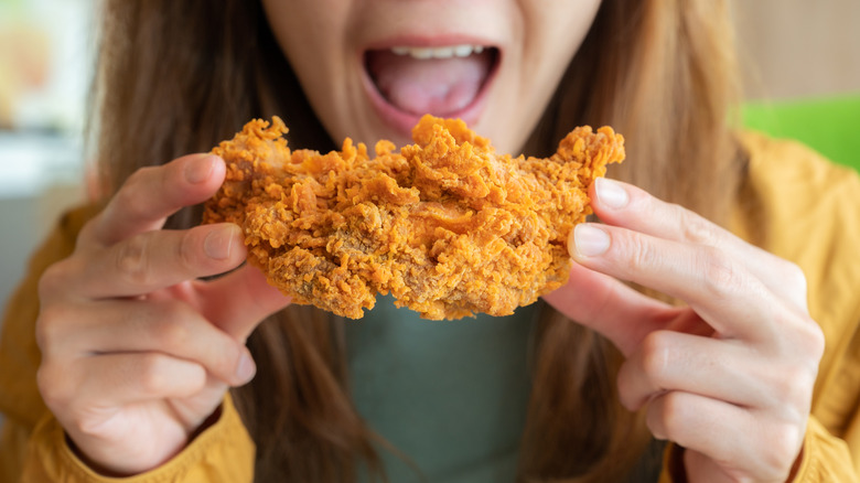A woman holding a piece of fried chicken