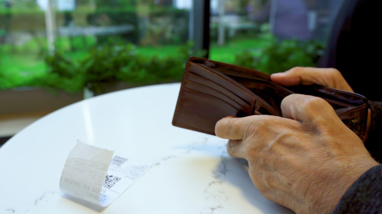 Opening an empty wallet at a restaurant with a check on the table.