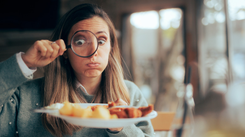 A diner looking at a plate of food through a magnifying glass.