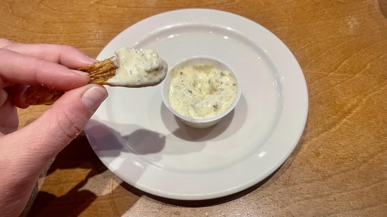 A hand holding a fry dipped in tartar sauce over a ramekin of tartar sauce.