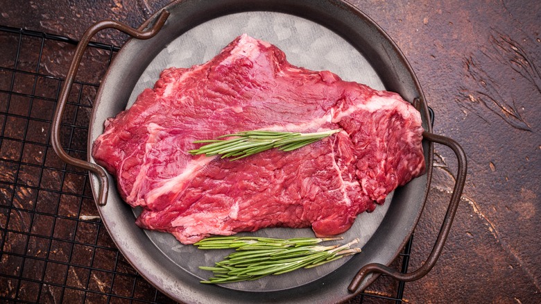 Raw hanger steak resting on a plate with herbs