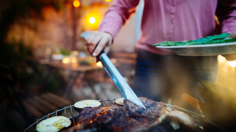 Woman pulling cooked meat from a grill with tongs
