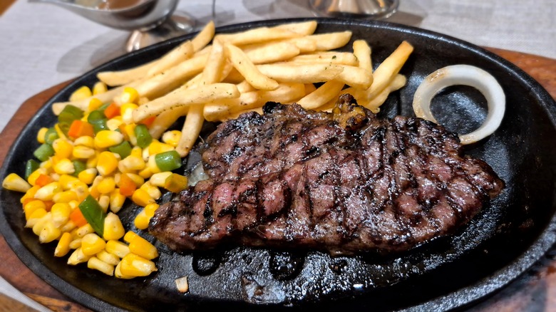 Grilled sirloin steak on a plate with vegetables and french fries