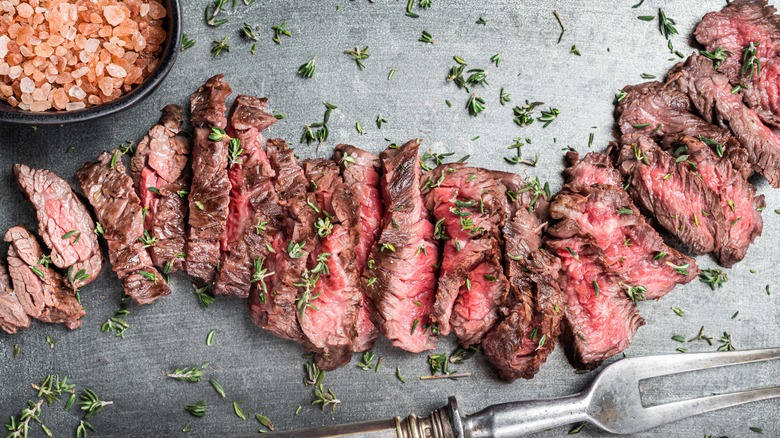 Cooked, sliced skirt steak resting beside salt on a cutting board