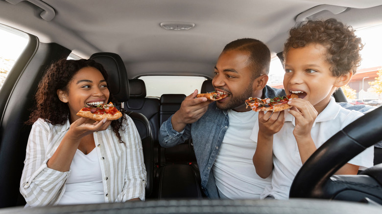 A family in their car enjoying a slice of pizza